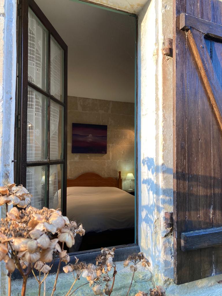 View through rustic shutters into the double bedroom of Gite La Maison du Frere, Moulin St Blaise